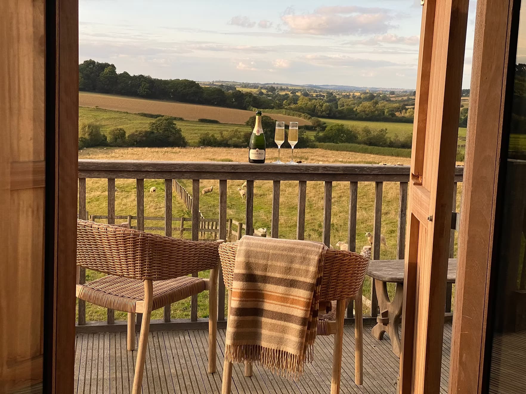 Two glasses of champagne on the balcony of The Hayloft at Barton at golden hour, looking out across the Cotswold hills
